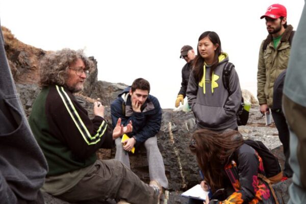 Photo of Dr. Murphy sitting on a rock outside and talking with students