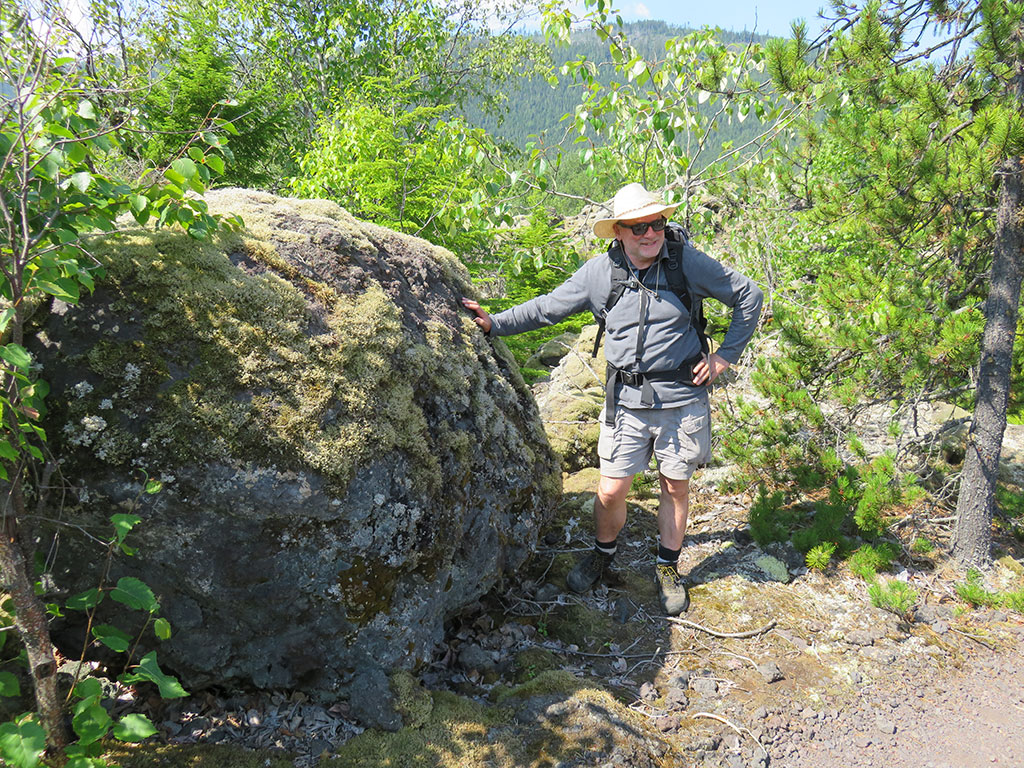 Man standing next to rounded lava rock in forest