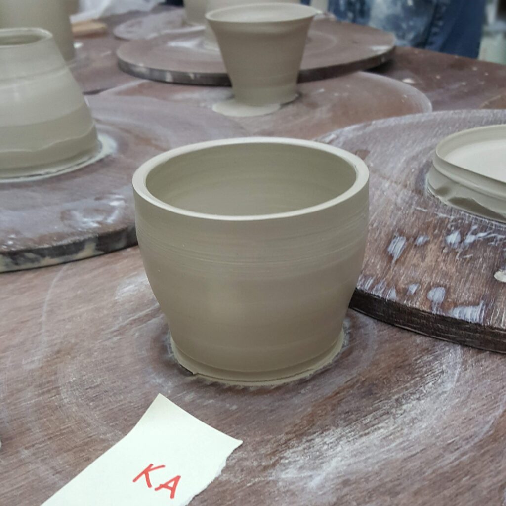 A clay mug with a piece of paper that reads "KA"