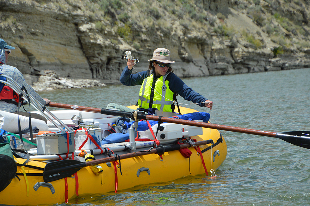 Two researchers take samples of water on a yellow, oar-equipped raft.